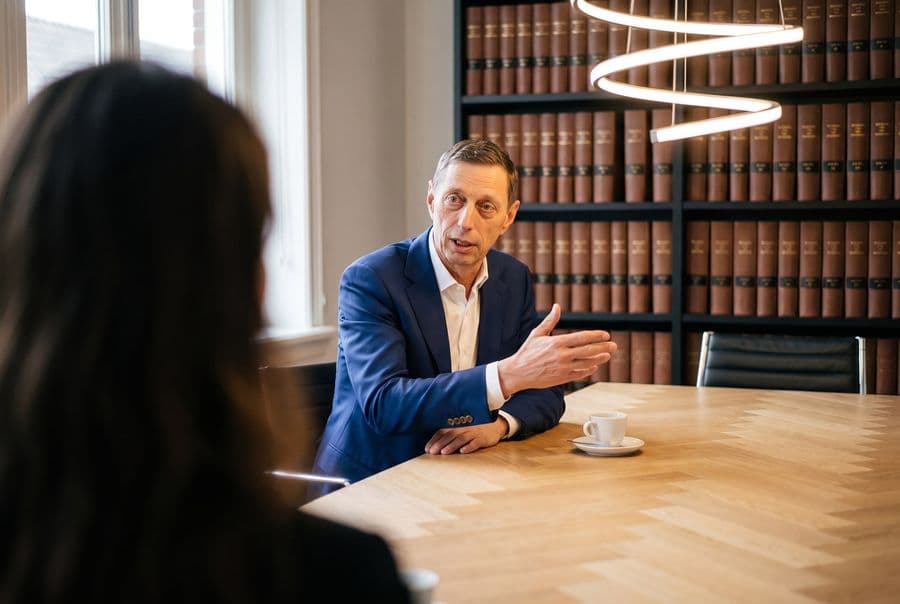 Advocaat licht een zaak toe aan tafel, met een boekenkast met juridische naslagwerken