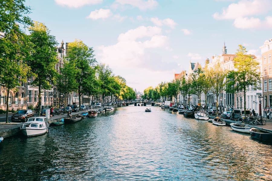 Amsterdamse gracht met bomen, bootjes en grachtenpanden