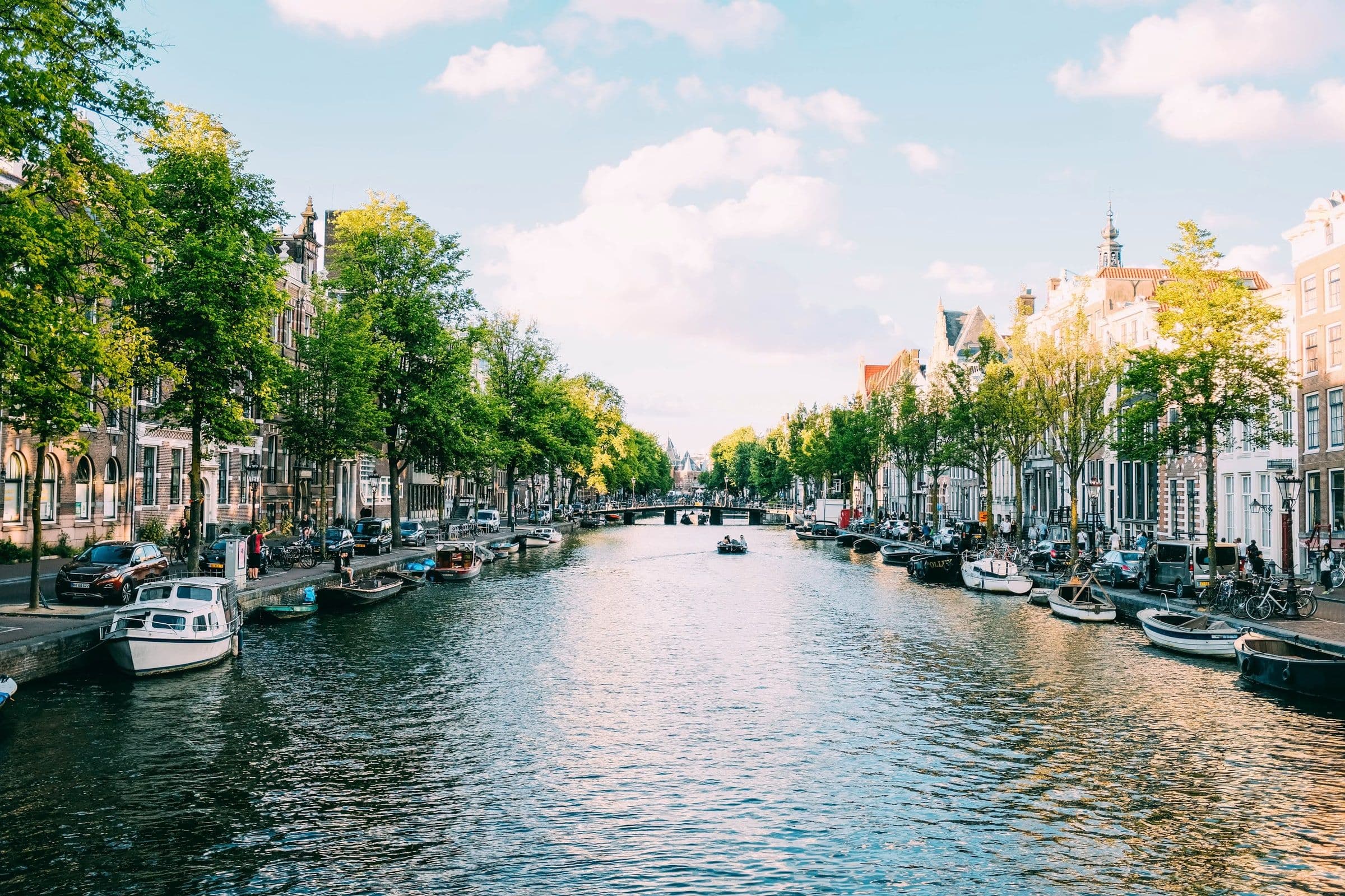 Amsterdamse gracht met bomen, bootjes en grachtenpanden